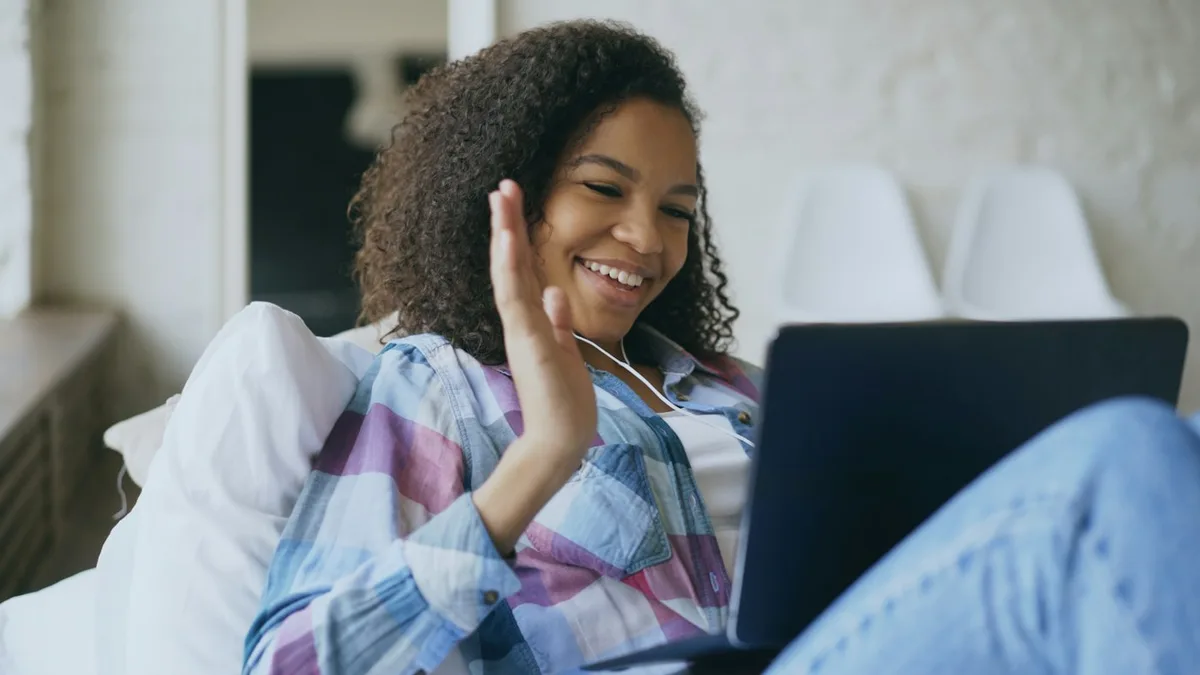 A woman waving hello on a video call from home