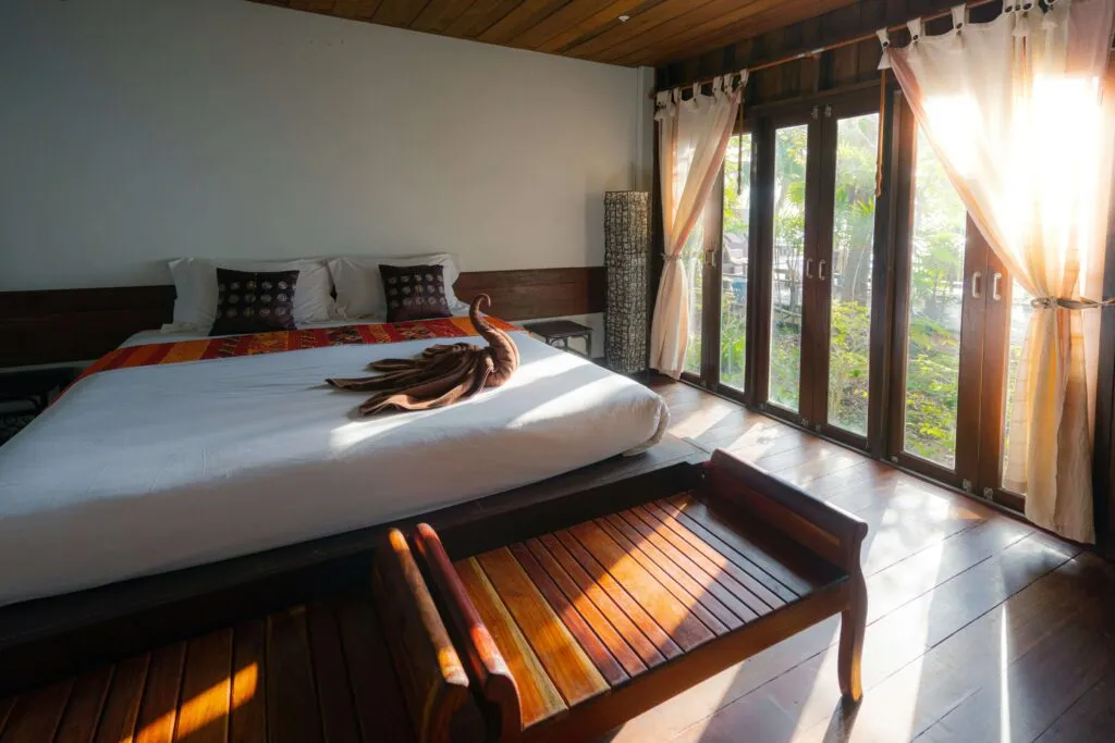 King-size bed with elegant swan towel decoration, set in a cozy room with a nature view through some large glass doors.