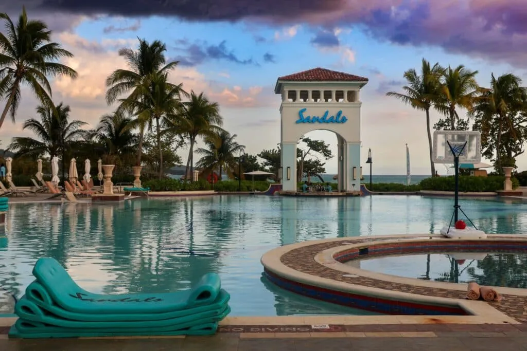 A stunning view of the pool area at Sandals Resorts, featuring crystal-clear water, comfortable lounge chairs, and lush tropical surroundings.
