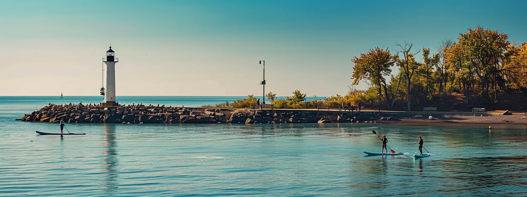 a serene beach scene at presque isle state park, with people paddleboarding near a picturesque pier and a historic lighthouse in the background.