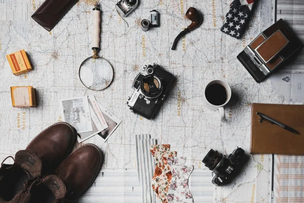A map surrounded by travel essentials, showcasing meticulous trip planning with things like clothing, a notebook, and cameras.
