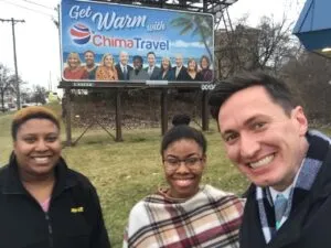 Robin and members of the Chima Travel team beside a company billboard